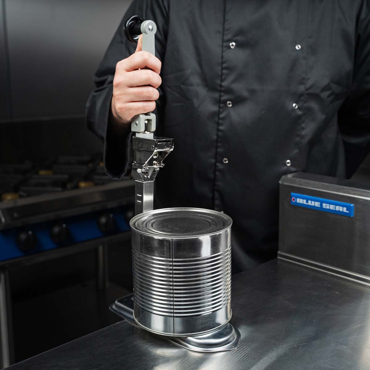 Chef lifting the handle of a bench tin opener with a can underneath