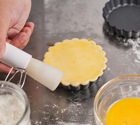 Chef using a pastry brush to add an egg wash to a tart