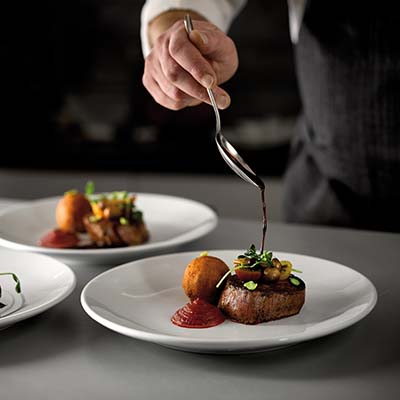 Person pouring sauce on a steak