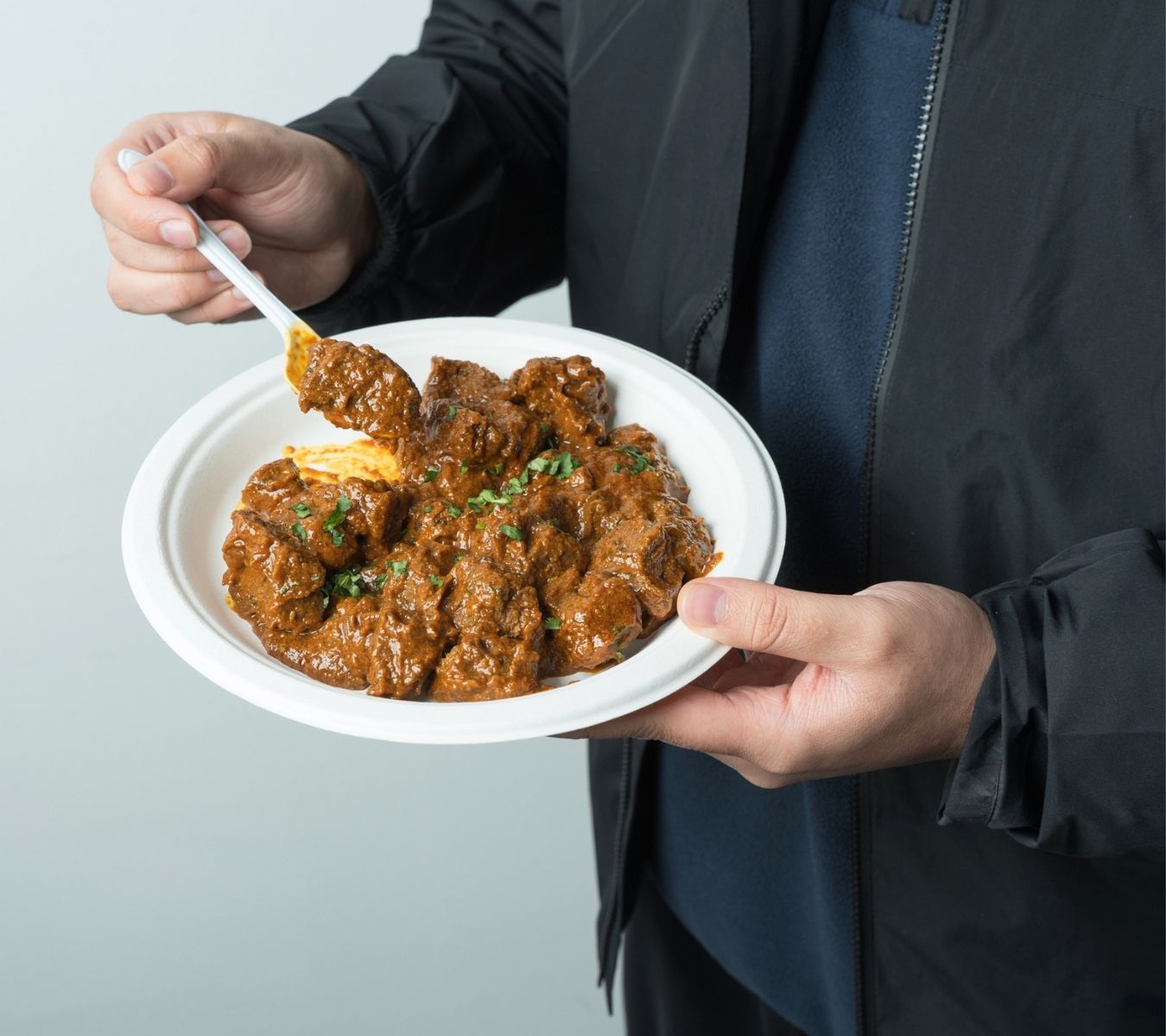 Person stood eating a curry off a bagasse plate