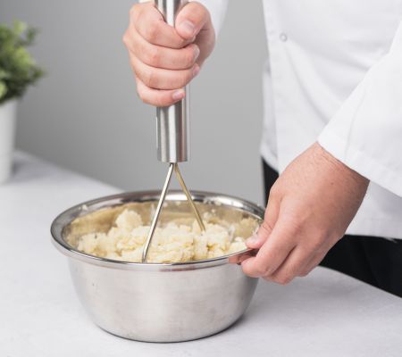 Chef using a masher to mash potatoes