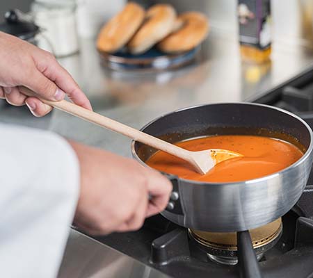 Chef using a wooden spoon to stir a sauce